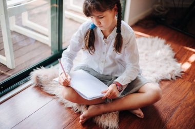 Pencere kenarındaki evde yazan küçük kızın kapalı bir portresi.