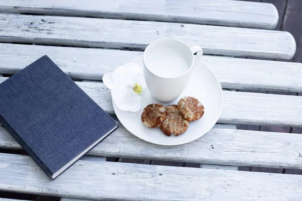 Tasse Milch Kekse Und Blaues Notizbuch Auf Weißem Holzgrund — Stockfoto