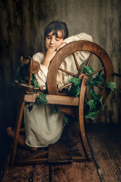 木製の背景にウール紡糸ホイールを持つ若い子供の女の子の屋内肖像画 — ストック写真