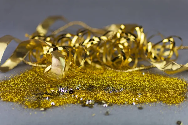 Golden sequins and metallic ribbon on neutral grey background. Copy space. Luxury celebration.