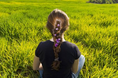 Genç kızıl saçlı bir kadın ve çiçeklerle örülmüş bir örgünün arkası ve başı. Yoga pozisyonunda çimlerin üzerinde oturmak. Farkındalık, meditasyon ve rahatlama. sahne