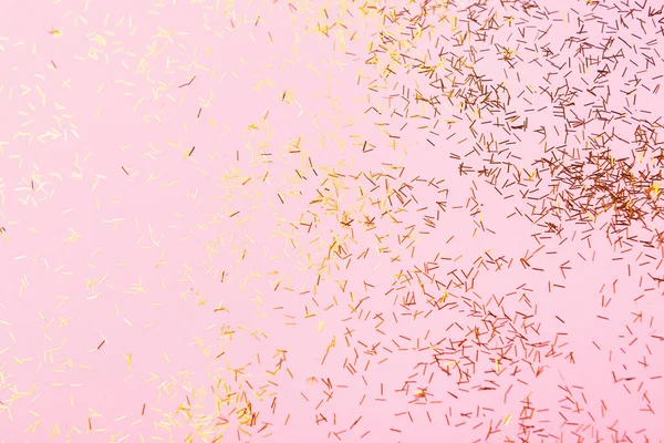 Falling small gold sparkles confetti on pastel pink background. Perfect festive background. Flat lay, top view. Copy space for your text.