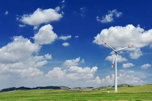 Wind generator turbine in a green field and blue sky with clouds — Stock Photo, Image