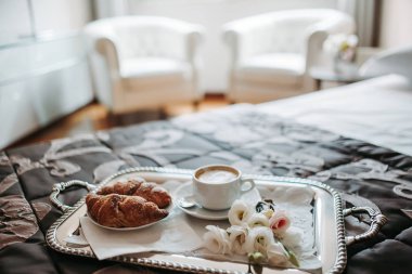 Kapuçino, kruvasan ve çiçek yatakta