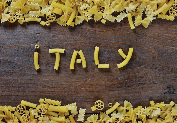 Italské těstoviny na dřevěné pozadí - Itálie slovo napsané s těstovinami — Stock fotografie
