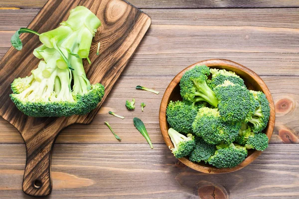 Ready to eat fresh raw broccoli is divided into inflorescences in a wooden plate and on a cutting board  on a wooden table. Healthy lifestyle, nutrition and zero waste concept. Top view