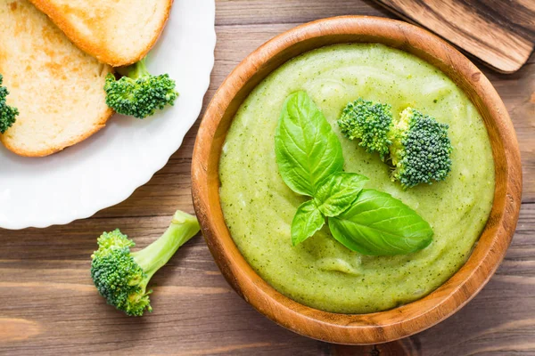 Ready to eat fresh hot broccoli puree soup with pieces of broccoli and basil leaves in a wooden plate on a wooden table. Close-up. Healthy eating and lifestyle. Top view