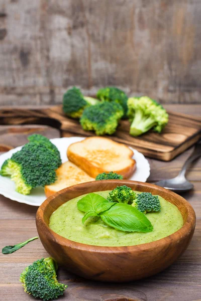 Ready to eat fresh hot broccoli puree soup with pieces of broccoli and basil leaves in a wooden plate and spoon  on a wooden table. Healthy eating and lifestyle.