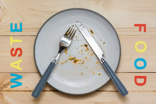 Stop wasting food. Dirty dinner plate and cutlery and the words \