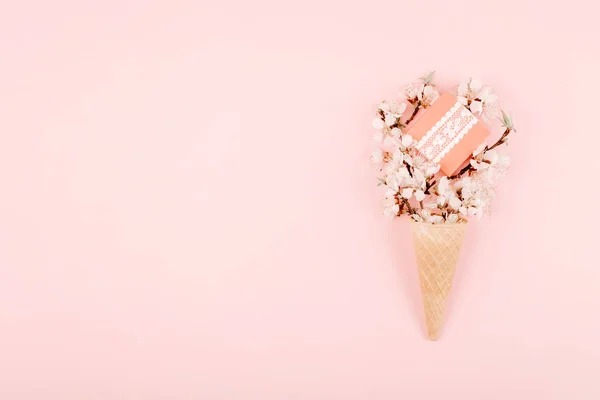 Минималистическая пастельная квартира, композиция с видом сверху с вафельным рожком мороженого, вишневые цветы и подарочная коробка на розовом фоне. Концепция минимального подарка — стоковое фото