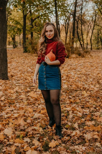 Jovem bela mulher sorridente com cabelos longos encaracolados segurando laranja abóbora halloween no outono parque amarelo árvores fundo. Outono outono halloween conceito — Fotografia de Stock