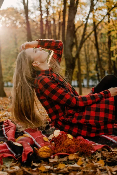 Belo retrato de outono de mulher jovem com cabelo loiro natural longo com folhas amarelas em vestido xadrez vermelho. Menina romântica ao ar livre desfrutando da natureza na luz do sol no pôr do sol — Fotografia de Stock