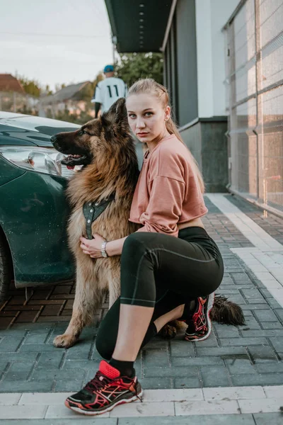 Joven hermosa chica deportiva con un perro grande pastor alemán esponjoso jugando en la calle de la ciudad. concepto de amor mascota —  Fotos de Stock