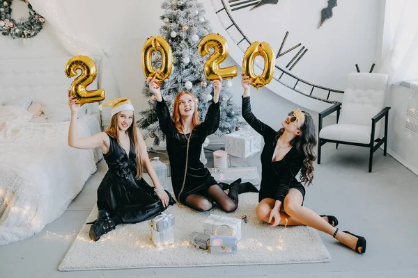 New Year Eve party. Celebrating of New Year. Three beautiful young girls with golden baloons 2020 celebrating new year. Young Woman in black cocktail evening dress Have Fun.