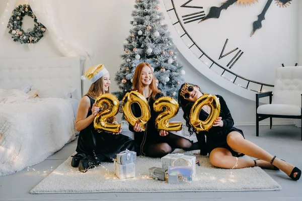 New Year Eve 2020 party celebration. Beautiful women celebrating new year 2020. Three happy girls in black metallic party dresses holding gold 2020 balloons