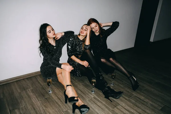 New Year\'s Eve, birthday celebration. After party, jet set, clubbing, nightlife concept. Three beautiful girls with glasses of champagne sit on the floor after celebrating party