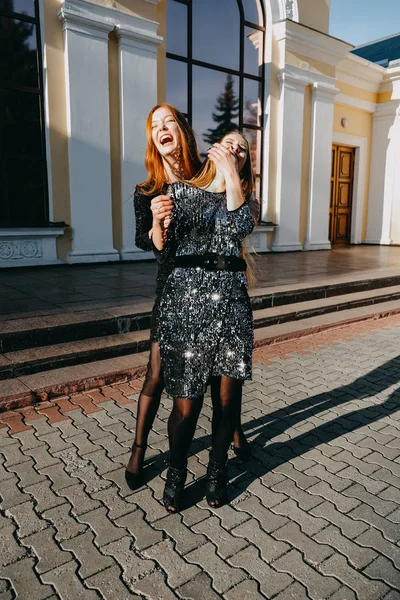 Idéias de roupa de cocktail de festa à noite. O que vestir. Tendência e moda. Duas belas gargalhadas jovens mulheres no brilho lantejoulas vestido ao ar livre. Loira e ruiva menina em vestidos de cocktail estilo de vida retratar — Fotografia de Stock