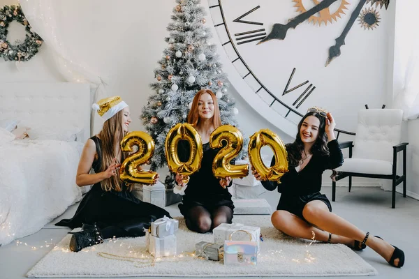 New Year Eve party. Celebrating of New Year. Three beautiful young girls with golden baloons 2020 celebrating new year. Young Woman in black cocktail evening dress Have Fun