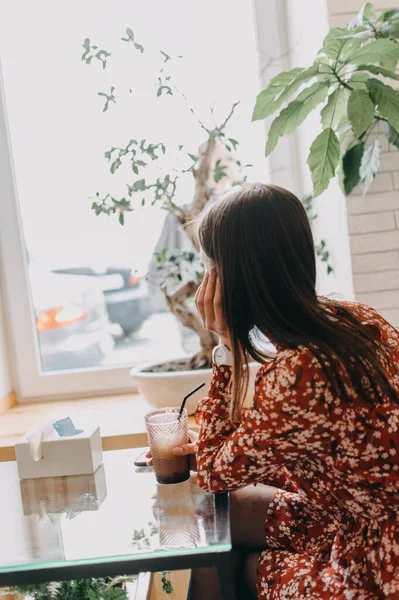 Задний вид юной брюнетки, сидящей в кафе одна, пьющей кофе и смотрящей в окно — стоковое фото