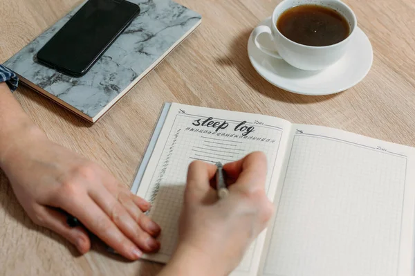 Woman hand with Sleep Log or Diary on table. How to Use a Sleeping Log to Diagnose Insomnia. Identify Sleep Disorders and Poor Sleep Habits.