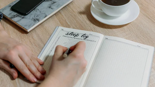 Masada uyku günlüğü ya da günlüğü olan bir kadın eli var. Uykusuzluk teşhisi için Uyuyan Kütük nasıl kullanılır? Uyku Bozukluklarını ve Kötü Uyku Alışkanlıklarını Tanımla.