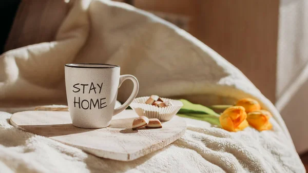 Stay home, Stay safe, Save Lives, quarantine, Help Stop Coronavirus concept. Anti-stress survival routine During Coronavirus Crisis. Cup with text Stay home and sweets on the bed in morning sun.