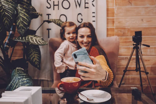 Online jobs for stay-at-home moms. Work From Home women with kids. Blogger girl and her little daughter have fun together. Young parenting blogger recording a video with her baby at home