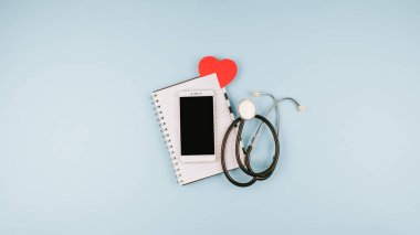 Teletıp veya tele-sağlık sanal ziyareti, video ziyareti, bilgisayarlı uzaktan doktor görüntülü sohbet konsepti, akıllı telefon, not defteri ve mavi arka planda steteskop..