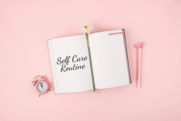 Self Care, wellbeing Routine, holistic set of self-care activities concept with open notebook, flower narcissus and alarm clock on pink background