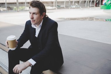 Yakışıklı iş adamı geleceğini düşünüyor. Elinde bir fincan kahve tutan ve sokakta oturan çekici yakışıklı adam. Yakışıklı adam takım elbise giyiyor. Sabah işe gitmeden önce kahve içer.