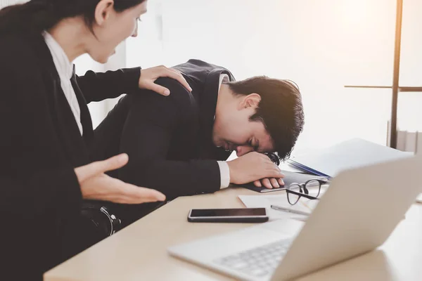 Businessman or colleagues guy sleeping during working with businesswoman. Workmate woman trying to wake up him but he still sleeping on desk at office. She get frustrated, unhappy, angry with lazy guy