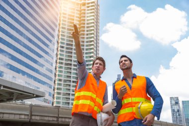 Mühendis ya da ustabaşı inşaat alanında çalışan işçi ya da mavi yakalı işçilerle birlikte çalışıyor. Patron mühendis ya da işveren arazi incelemesi için işaret binasını işaret ediyor. İşçilere açıklayın.