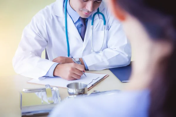 Doctor working in medical office or doctor office at hospital. Doctor writing and analyzing symptom of patient when patient telling patient illness. Doctor hang stethoscope on neck. Healthcare concept