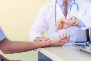 Doktor hastanın nabzını parmaklarıyla ölçer, hastaların bileğine dokunur. Doktor kol saatini kontrol ediyor. Klinikteki doktor masasında çalışıyorum. Genel doktor, hastayı kontrol edin..