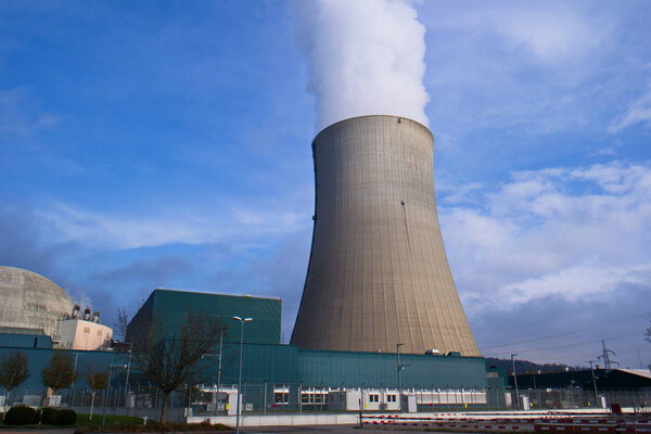 Outside wide angle shot of Gosgen Nuclear Power Plant in Switzerland on a nice autumn day with blue sky and white clouds huge furnace giving out massive amounts of steam