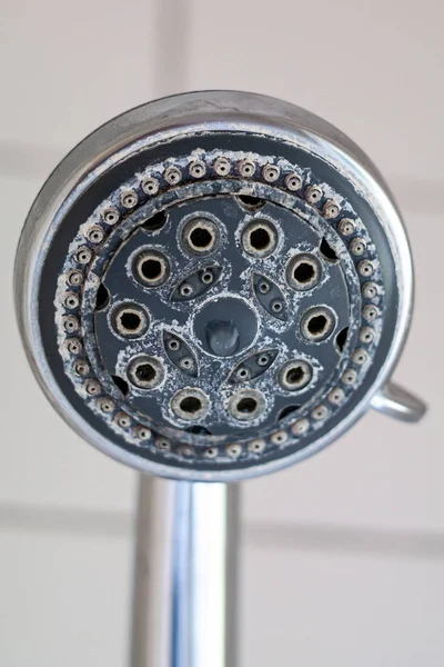 Silver round shower head with hard water deposit all around the