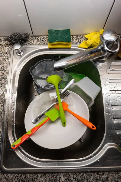 Kitchen sink full of dirty dishes cleaning sponge wire mesh and utensils top view 2020