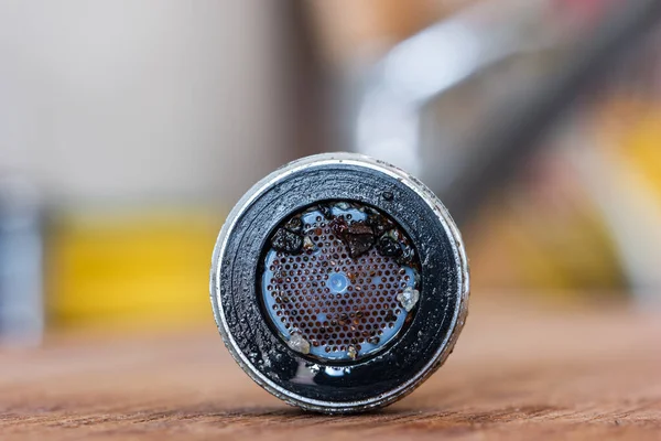 Eski tıkanmış musluk havalandırması, sert su kaynaklı kum ve kalsiyum tortularıyla dolu. Mutfağa yakın makro çekim, 2020 alanının sığ derinliği ile izole edilmiş.