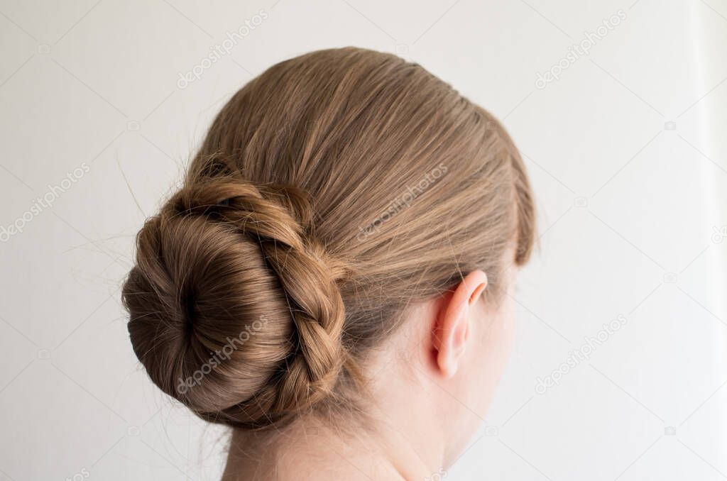 Caucasian young woman with her hair in a french bun with frizzy loose hairs seen from behind not recognizable 2020