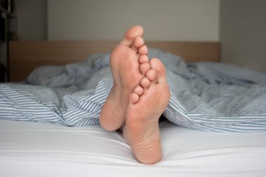 Beyaz erkek ayakları yatakta yorgandan sarkıyor. Saha manzarasının derinliği 2020.
