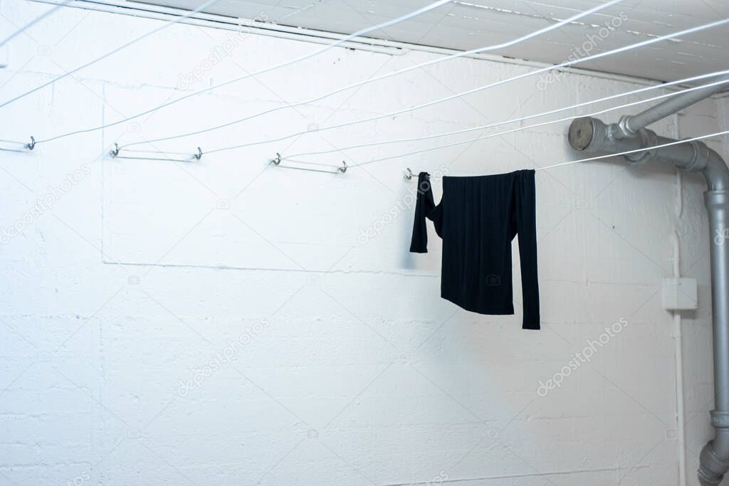 Single black long sleeved blouse hanging out to dry on a string inside a common use laundry room 2020