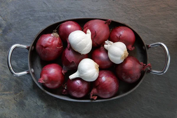 Red onions and garlic in old cooking tray on slate