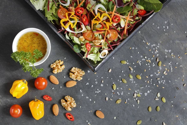 Salad ingredients with lettuce, cabbage, nuts and seeds and red  and yellow hot pepperson slate from above