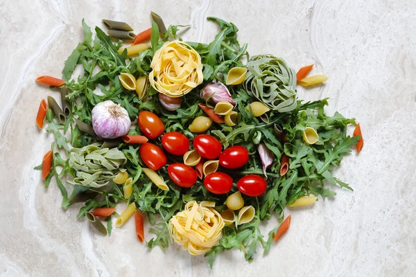 与李子西红柿和大蒜的火箭芝麻菜与面条和通心粉面食 Tricolore 意大利食物在大理石桌上的配料 — 图库照片