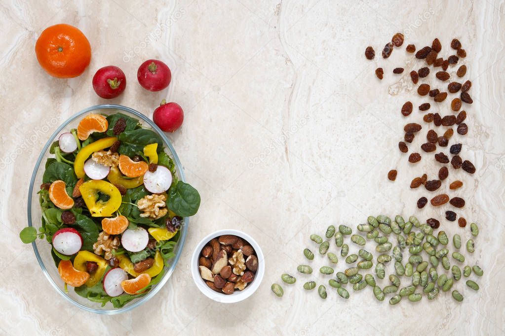 Healthy vegan salad with radish, nuts, yellow pepper and sultanas on marble with copy space in middle