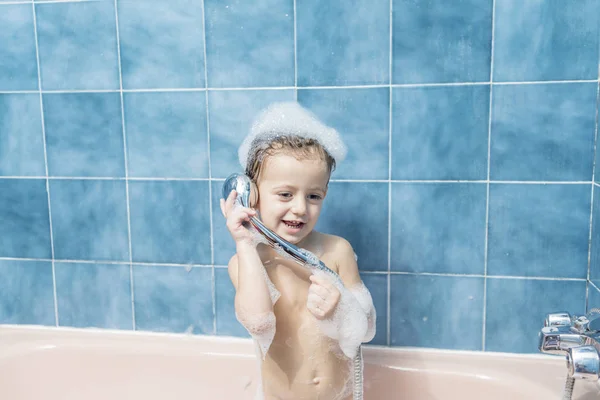 Köpük ve duş başlığı ile oynarken kafa onun dolu ile renkli fotoğraf gülümseyen bir çocuğun banyoda.