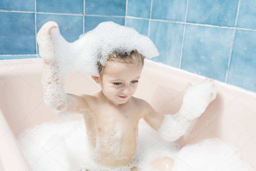Color photography of a smiling child playing in the bath with his head full of foam.
