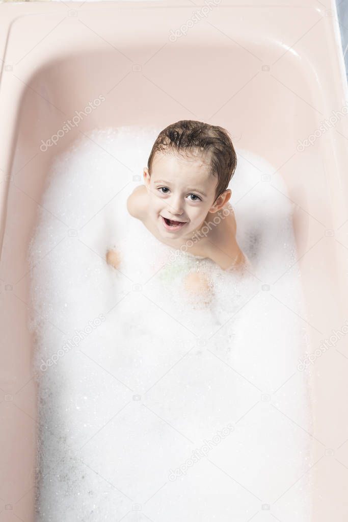 Color photography of a smiling child in a bubble bath.