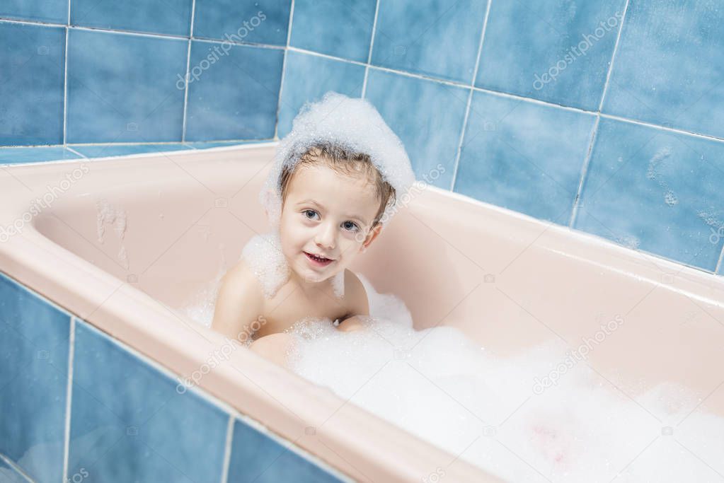 Color photography of a smiling child playing in the bath with his head full of foam.