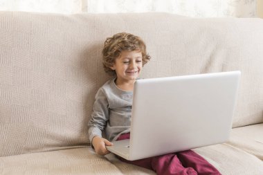 Çocuk kanepede oturup dizüstü bilgisayar izliyor..